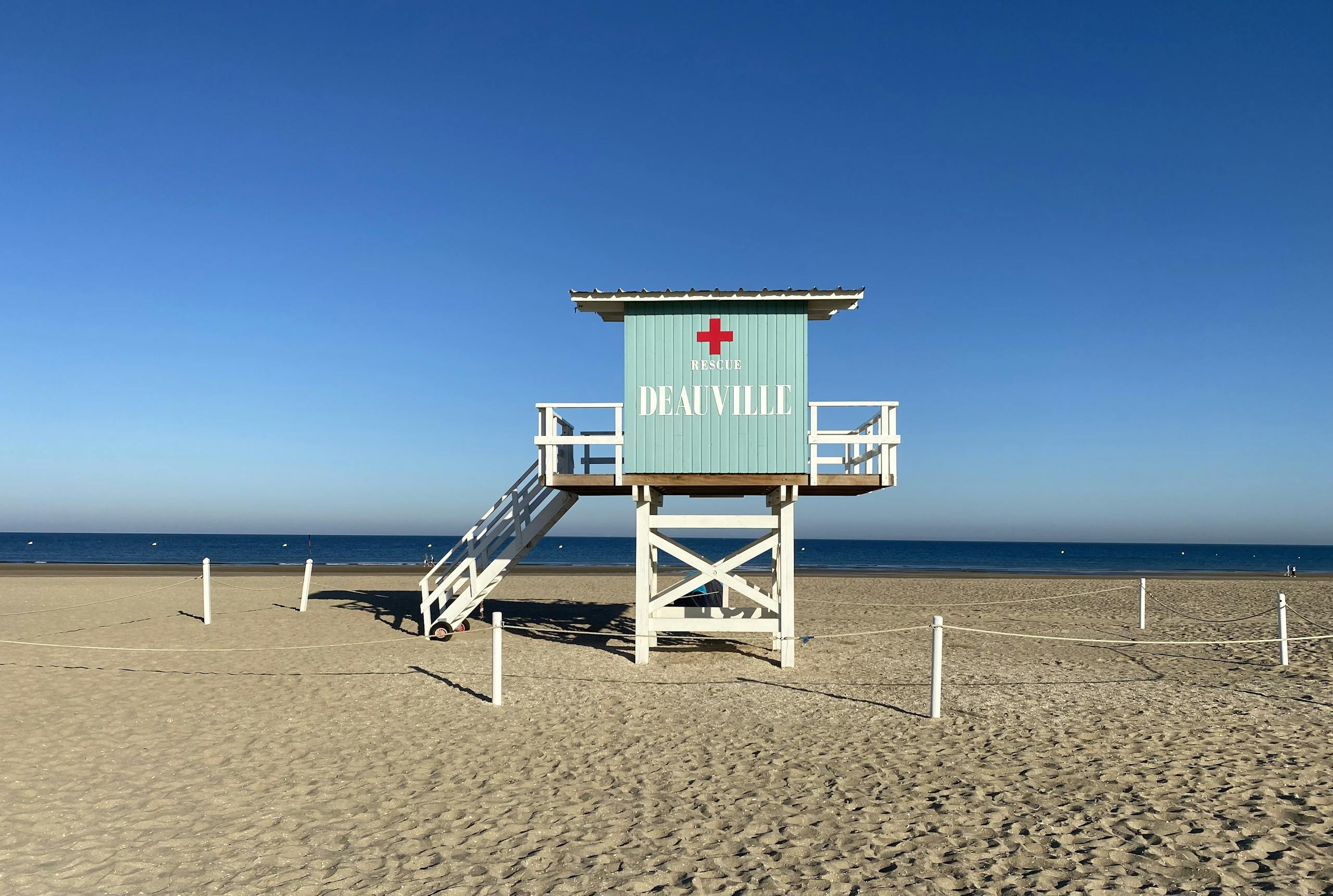 Peaceful scene of a lifeguard tower on Deauville Beach with clear skies and calm sea.